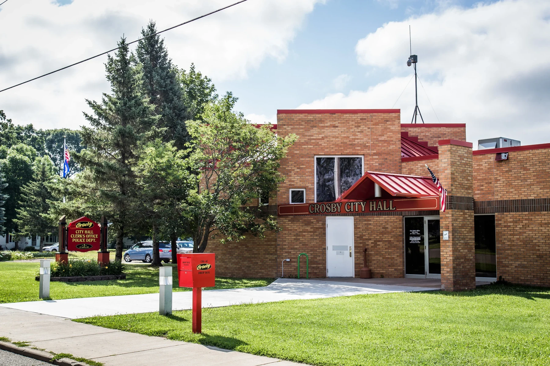 Crosby City Hall, a brick municipal building with a red metal awning reading Crosby City Hall, a City of Crosby drop box, and a sign for the Clerk's Office and Police Department