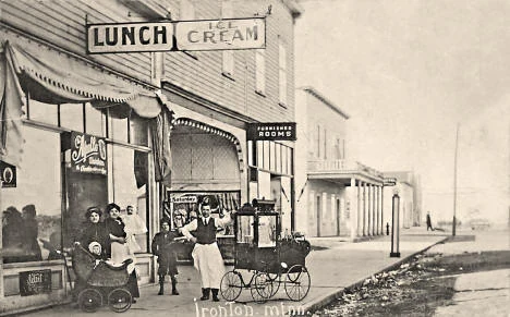A 1916 postcard photograph of Main Street in Ironton, Minnesota, showing a lunch counter and ice cream shop storefront, pedestrians, and baby carriages