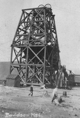 A black-and-white photograph of the Davidson No. 1 mine headframe on the Cuyuna Range, with two workers walking near its base